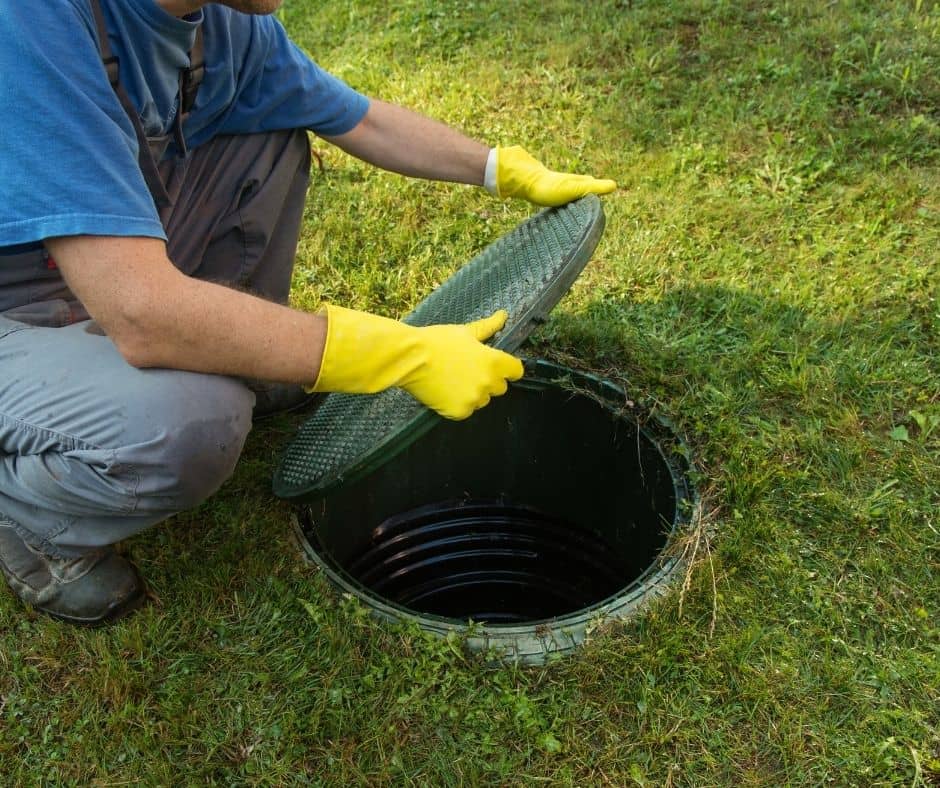 Close-up of hands opening a septic tank lid to access the tank