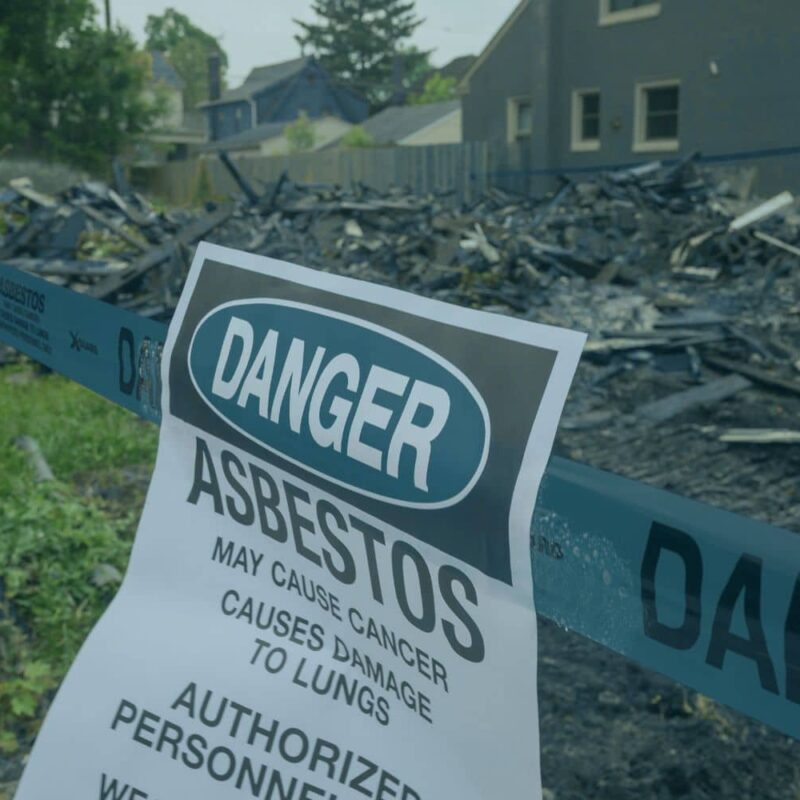 An asbestos danger sign posted at a residential home demolition site, warning about hazards like hidden asbestos walls.