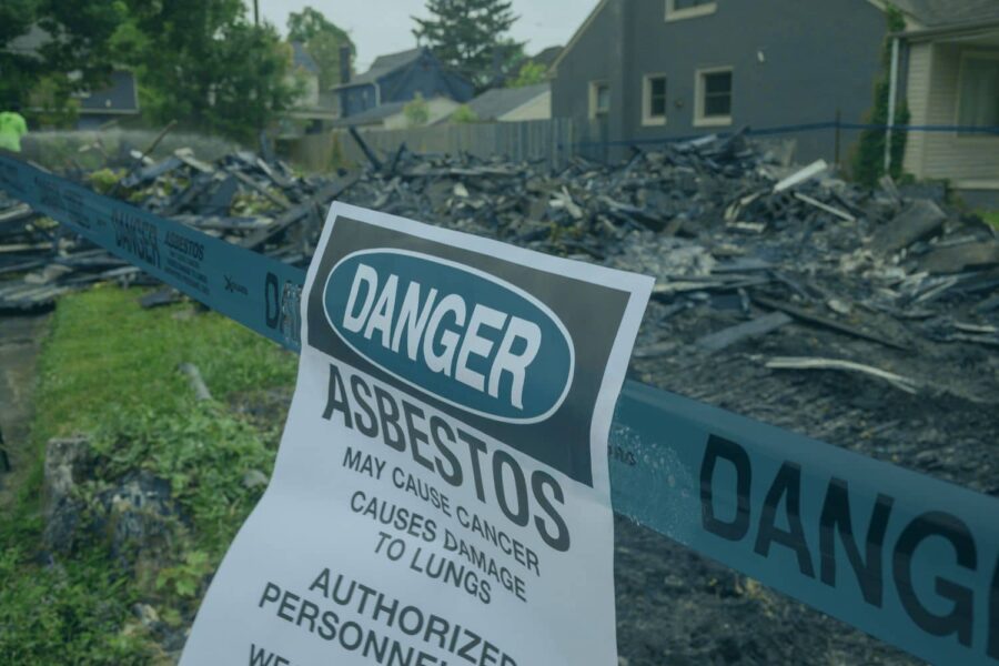 An asbestos danger sign posted at a residential home demolition site, warning about hazards like hidden asbestos walls.